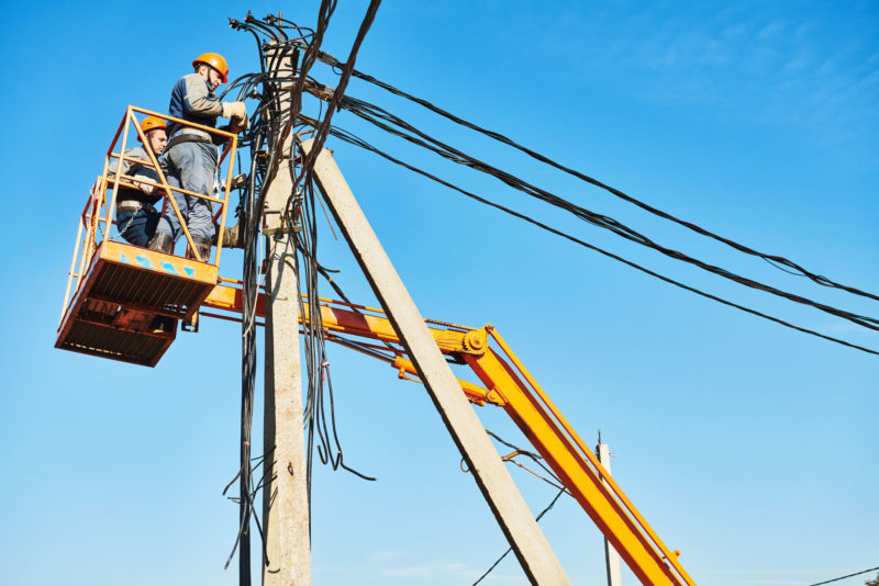 Electrician lineman repairman worker at climbing work on electric post power pole. Electrification.